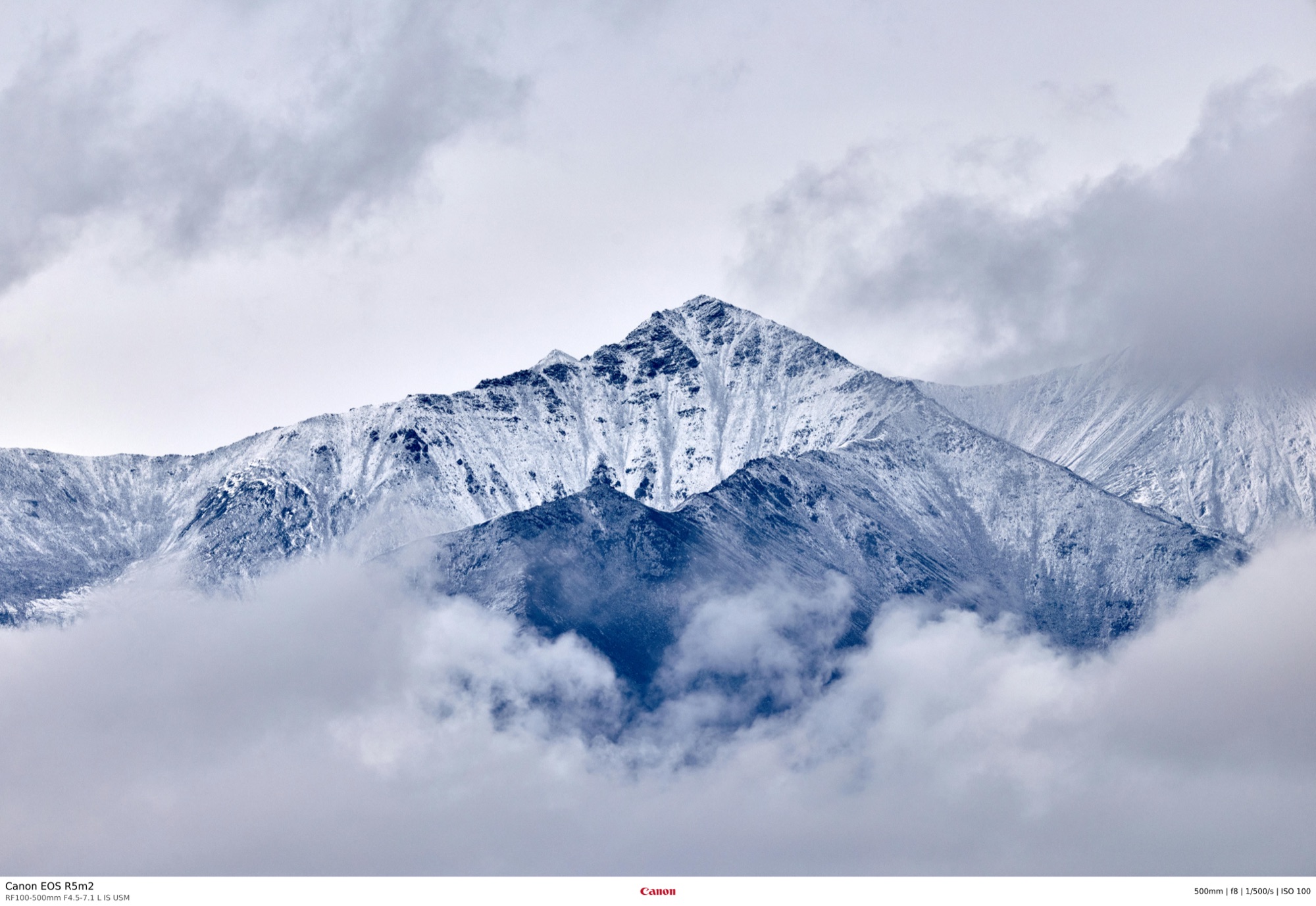Snow-dusted mountain ridge emerging from a sea of cloud, shot on a long lens